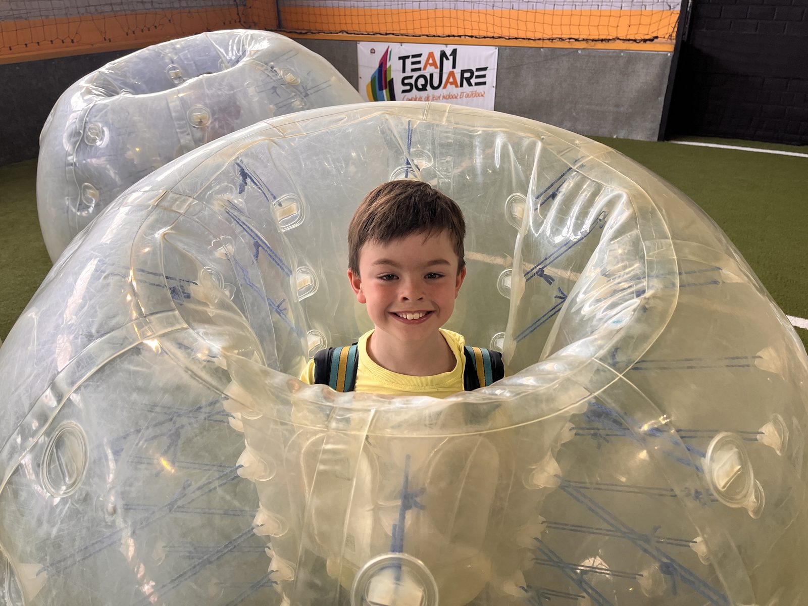 Un enfant dans une bulle de bubble foot, sourire aux lèvres